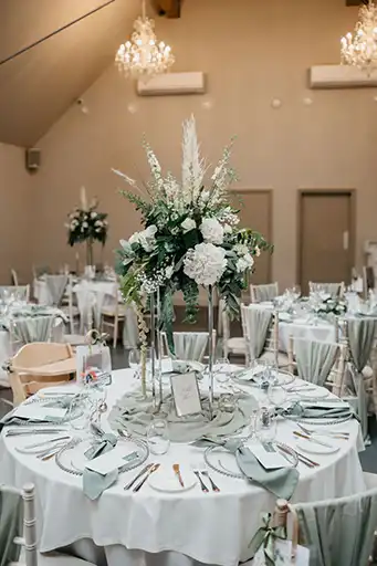 Elegant round table with tall floral centrepiece and sage decor at a Cotswolds wedding reception.