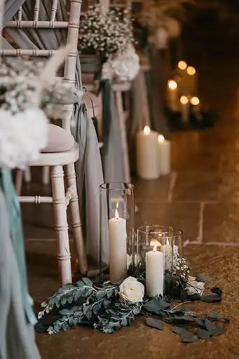 Romantic aisle decor with candles and greenery designed by a wedding florist in the Cotswolds.