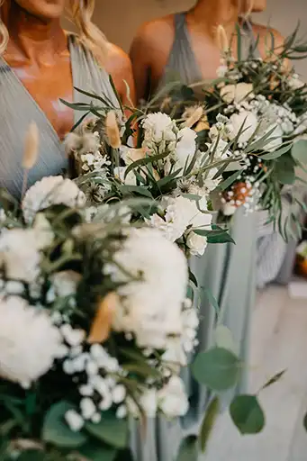 Bridesmaids' bouquets with white blooms and greenery tied with sage ribbons.