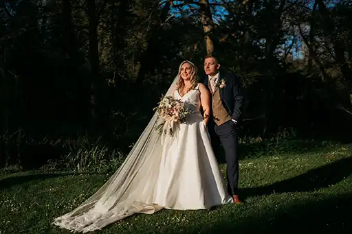 Bride and groom posing outdoors in soft evening light with lush bouquets at The Mill Barns.