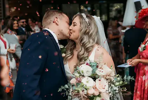 Bride and groom sharing a kiss surrounded by confetti at their Mill Barns wedding.